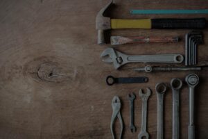 Assorted hand tools including hammer, adjustable wrench, wrenches, pliers, and hex keys on a wooden workbench surface.