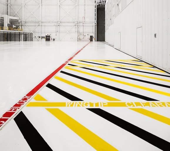 Aviation hangar floor with safety markings, including yellow and black stripes, red lines, and caution tape, emphasizing the importance of floor marking for operational safety and FOD awareness.